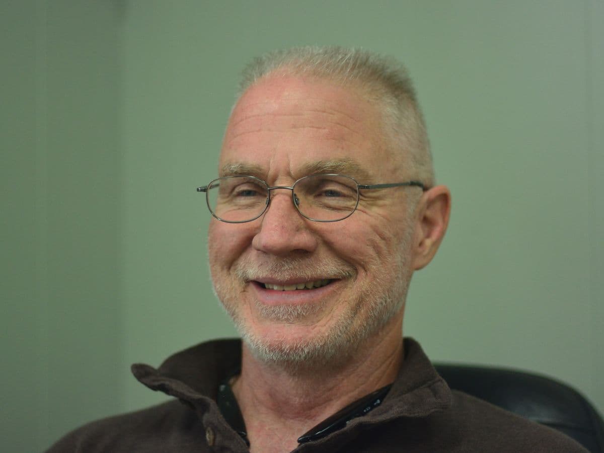 Eric Sumpter, owner of Mile Hybrid Automotive, smiling, with short grey hair, wire glasses and a brown pullover